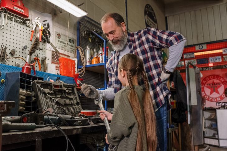 Mees õpetab töökojas oma tütrele kuidas kasutada tööriistu.