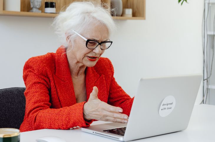 Punase pintsaku ja valgete juustega vanem naine vaatab segaduses sülearvuti poole.