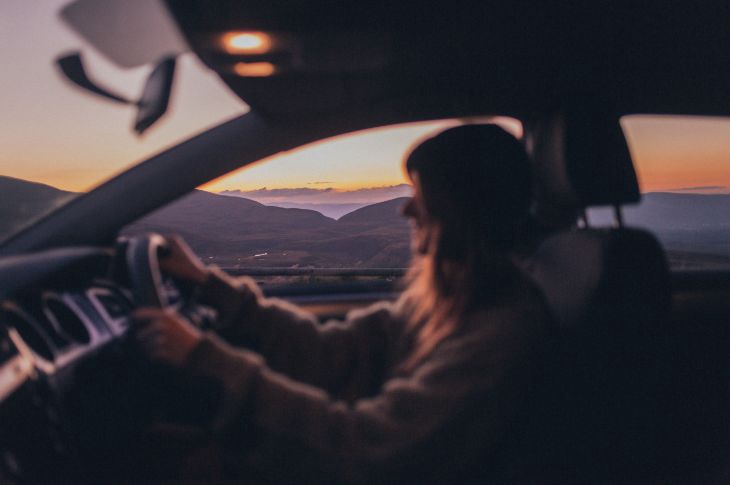 Naine sõidab autoga, auto aknast paistab päikeseloojang.