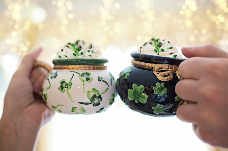 kaks tassi iirikohvi serveeritud savitassidesse millel ristikheina disain, vahukoor on kaunistatud roheliste helvestega 
